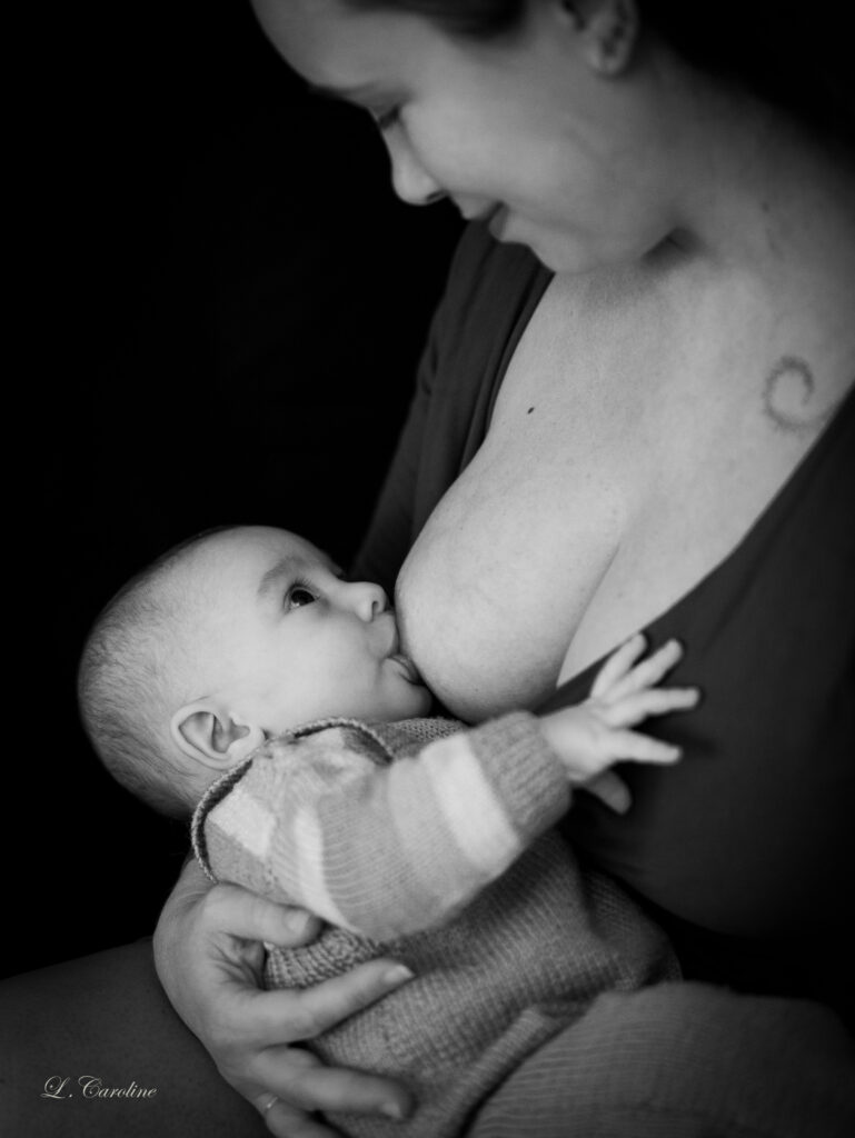 Photo de Caroline Lafargue, MCM Photographe représentant un bébé en train de téter. Il a une salopette tricoté et un pull rayé. Il regarde sa mère et ce regard est réciproque. La photo est en noir et blanc.